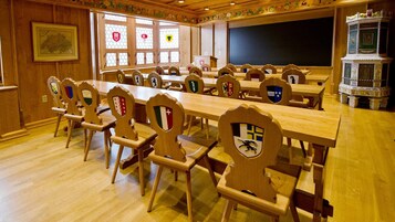 A conference room with long tables and chairs, each with a shield emblem, a blackboard, and a decorative cabinet.