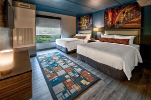 A hotel room with two beds, a large window, a modern air conditioning unit, and a colorful abstract painting on the wall.
