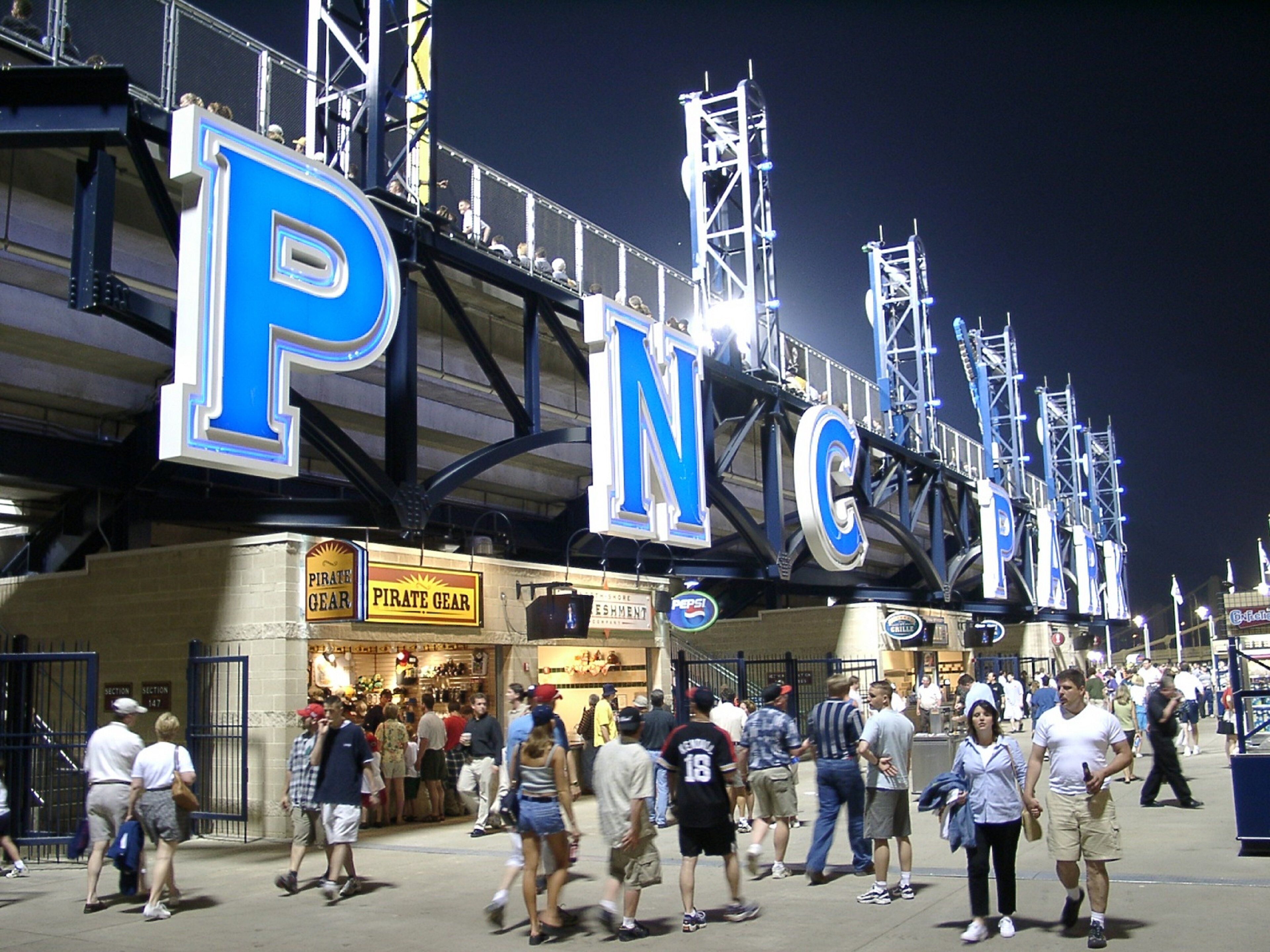 A stadium with large illuminated letters spelling 'PNC' and a crowd of people walking on the walkway.