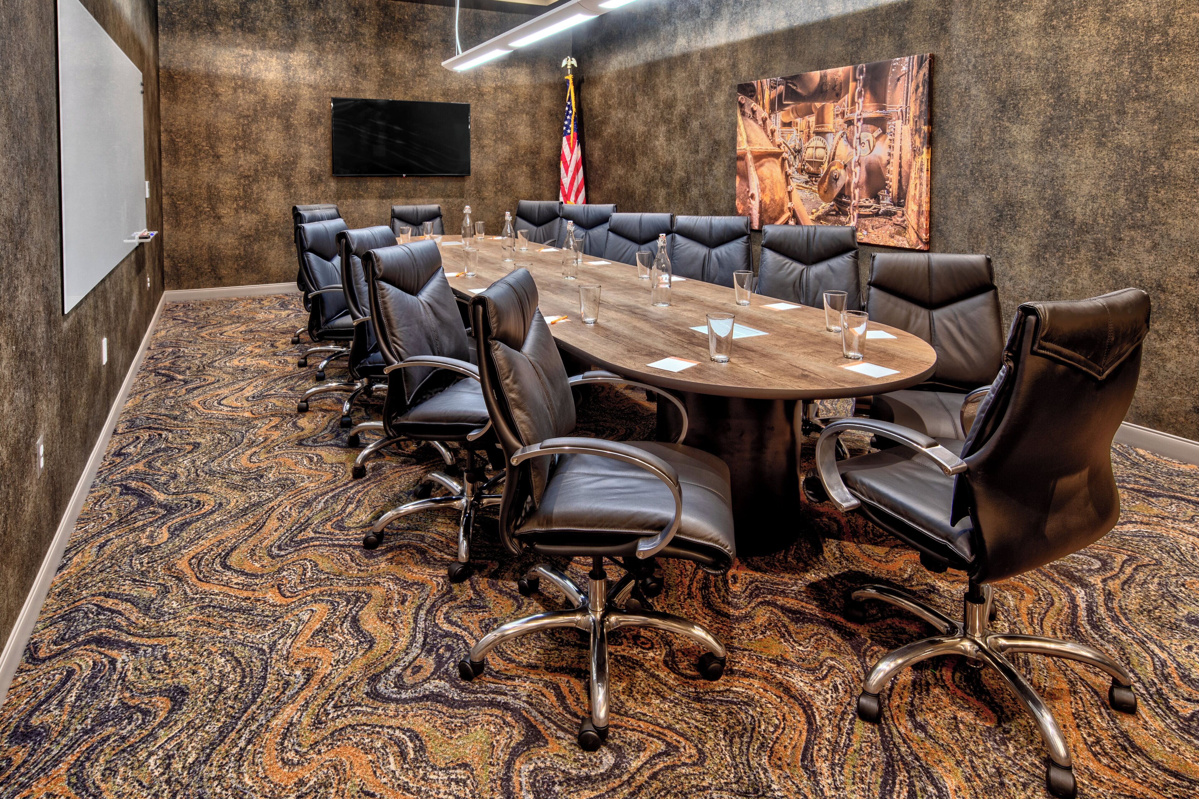 A conference room with a large oval table, black leather chairs, a flag, and a painting on the wall.
