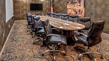 A conference room with a large oval table, black leather chairs, a flag, and a painting on the wall.