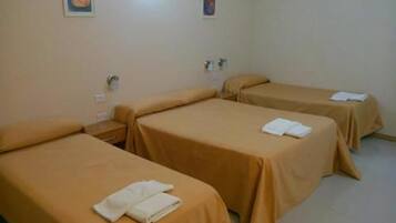 A hotel room with three single beds, each with a white towel folded on top.