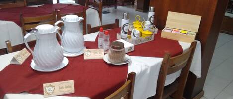 Una mesa de comedor con jarras blancas, un recipiente amarillo y una caja pequeña con la etiqueta 'Cafe - Coffee'.