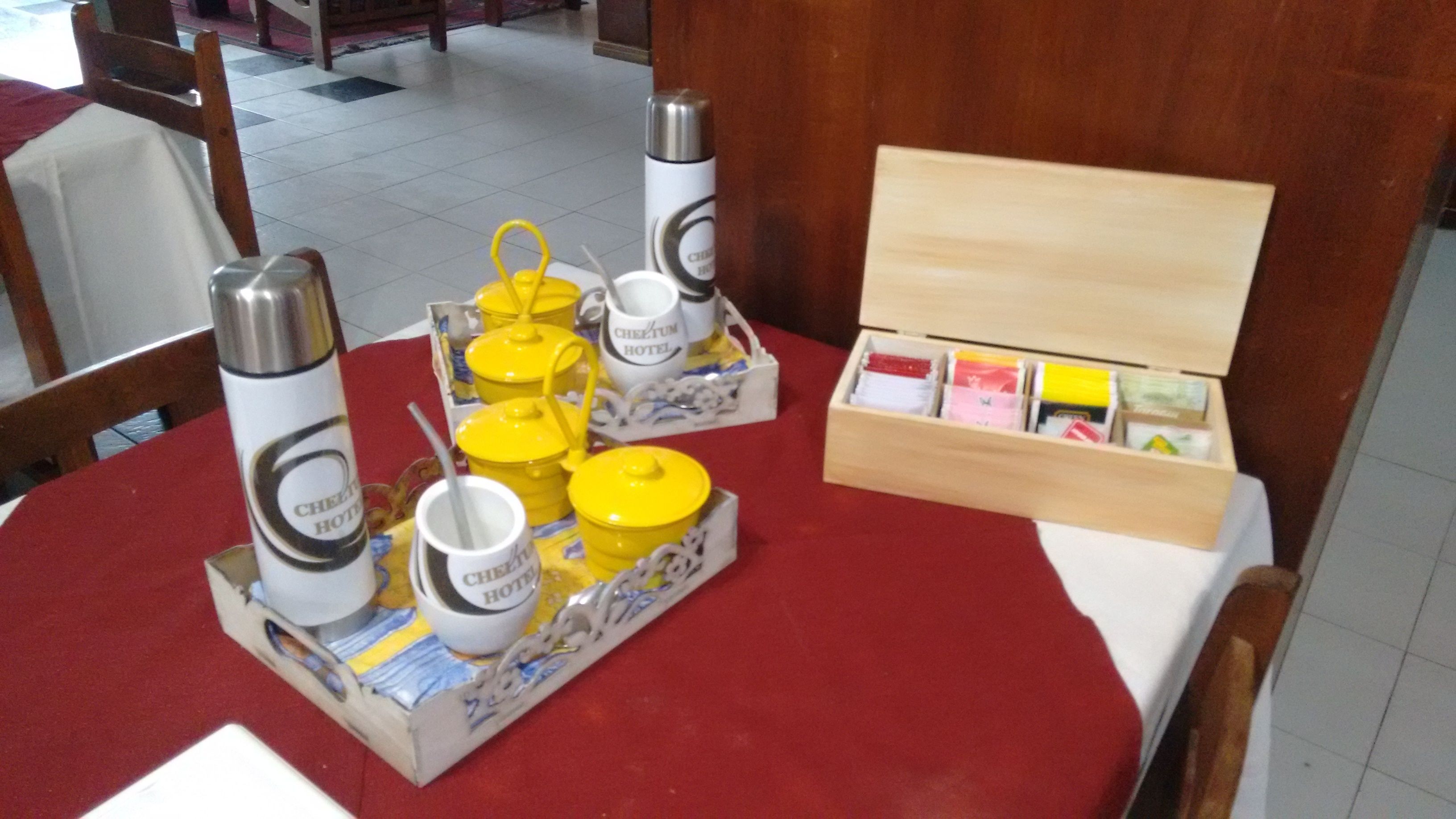 Un tavolo d'hotel apparecchiato con teiere gialle, tazze e una scatola di bustine di tè.
