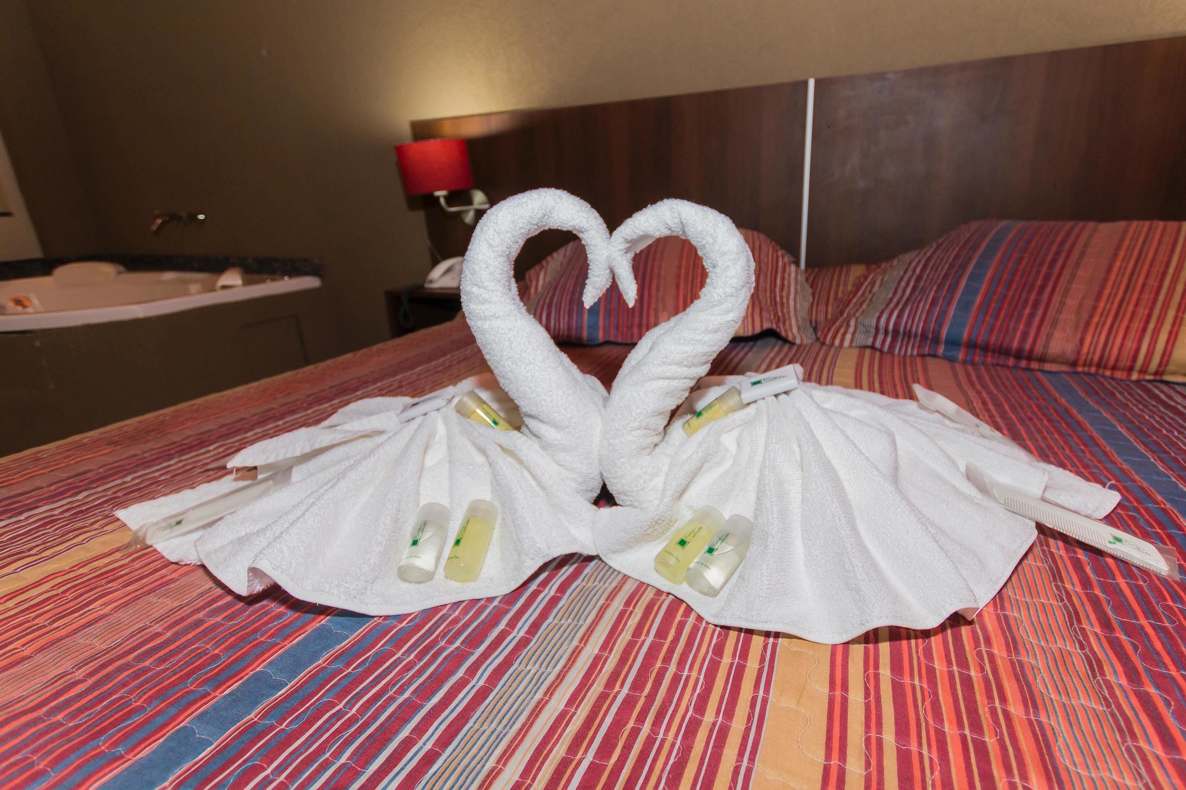 A hotel room with a bed featuring a heart-shaped towel arrangement and toiletries.