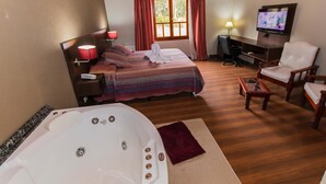 Habitación de hotel con una cama grande, zona de estar con televisor, suelo de madera y bañera de hidromasaje.