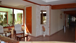 Un salón amplio con un gran ventanal, una puerta de madera y un suelo de baldosas blancas.