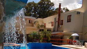 Una piscina con agua azul cristalina, una fuente de agua y un edificio con ventanas rojas y una chimenea al fondo.