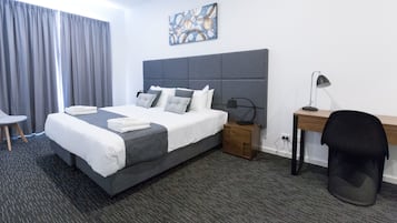 A hotel room with a large bed, a desk, a chair, a nightstand, and a painting on the wall.