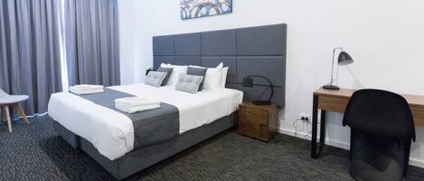 A hotel room with a large bed, a desk, a chair, a nightstand, and a painting on the wall.