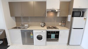 A compact kitchen with a dishwasher, washing machine, oven, microwave, and refrigerator. - The Palms Apartments (Kent Town)