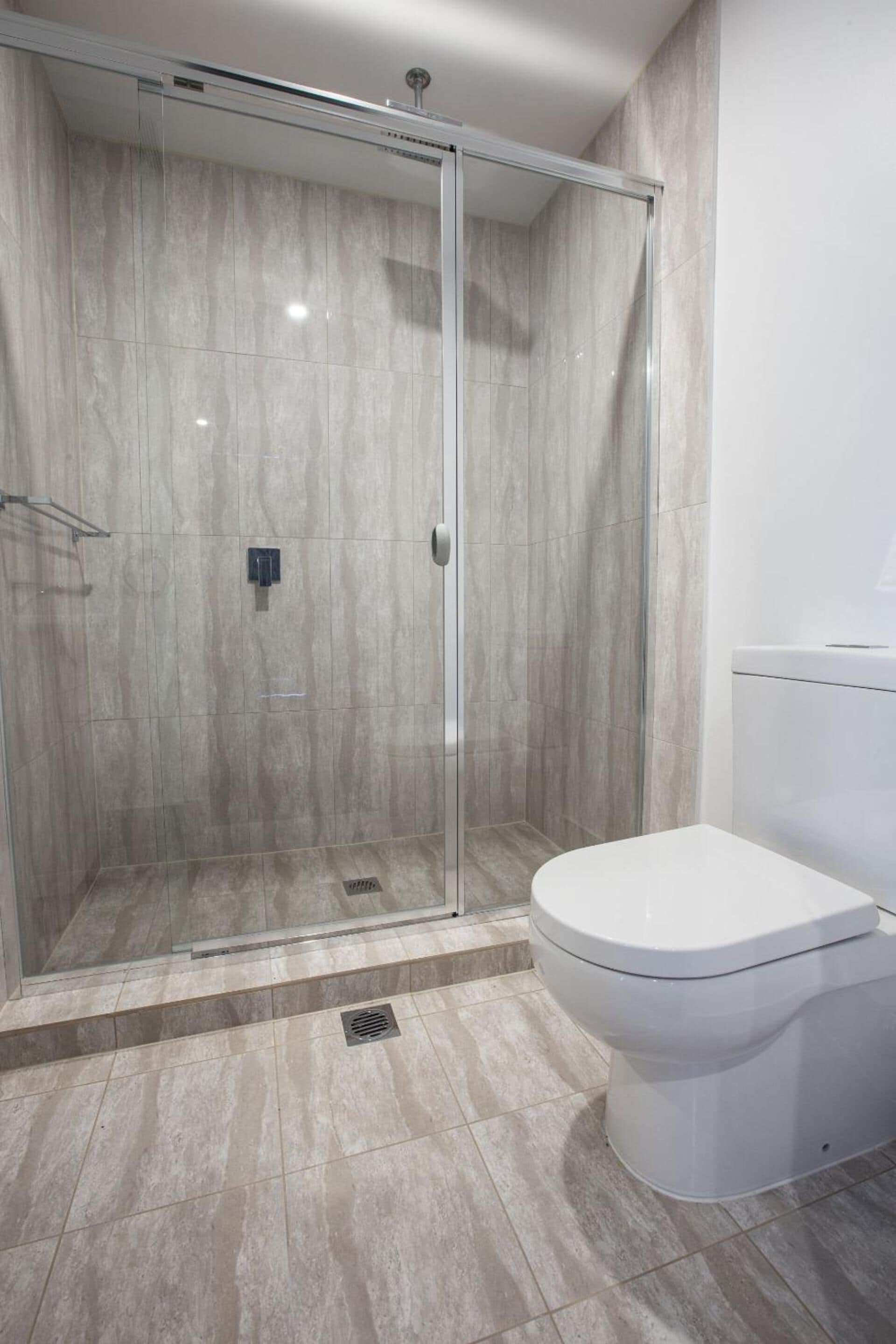 A modern bathroom with a glass-enclosed shower, a white toilet, and a marble-tiled floor.