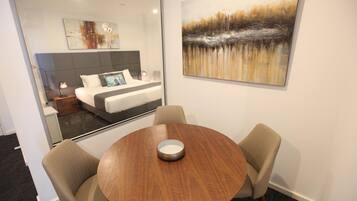 Una habitación de hotel con cama, mesita de noche, lámpara y una mesa redonda de madera con dos sillas.
