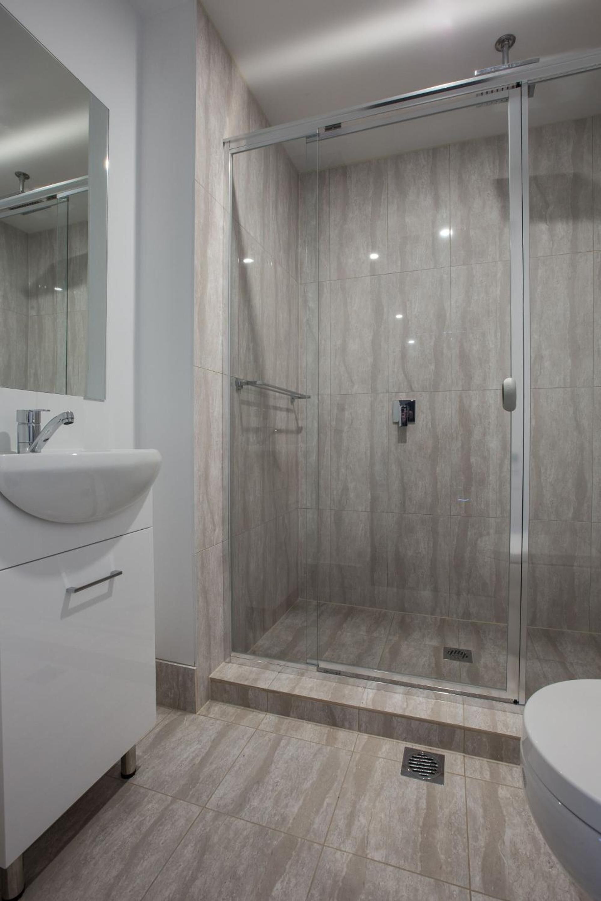 A modern bathroom with a glass-enclosed shower, a white sink, and a toilet.