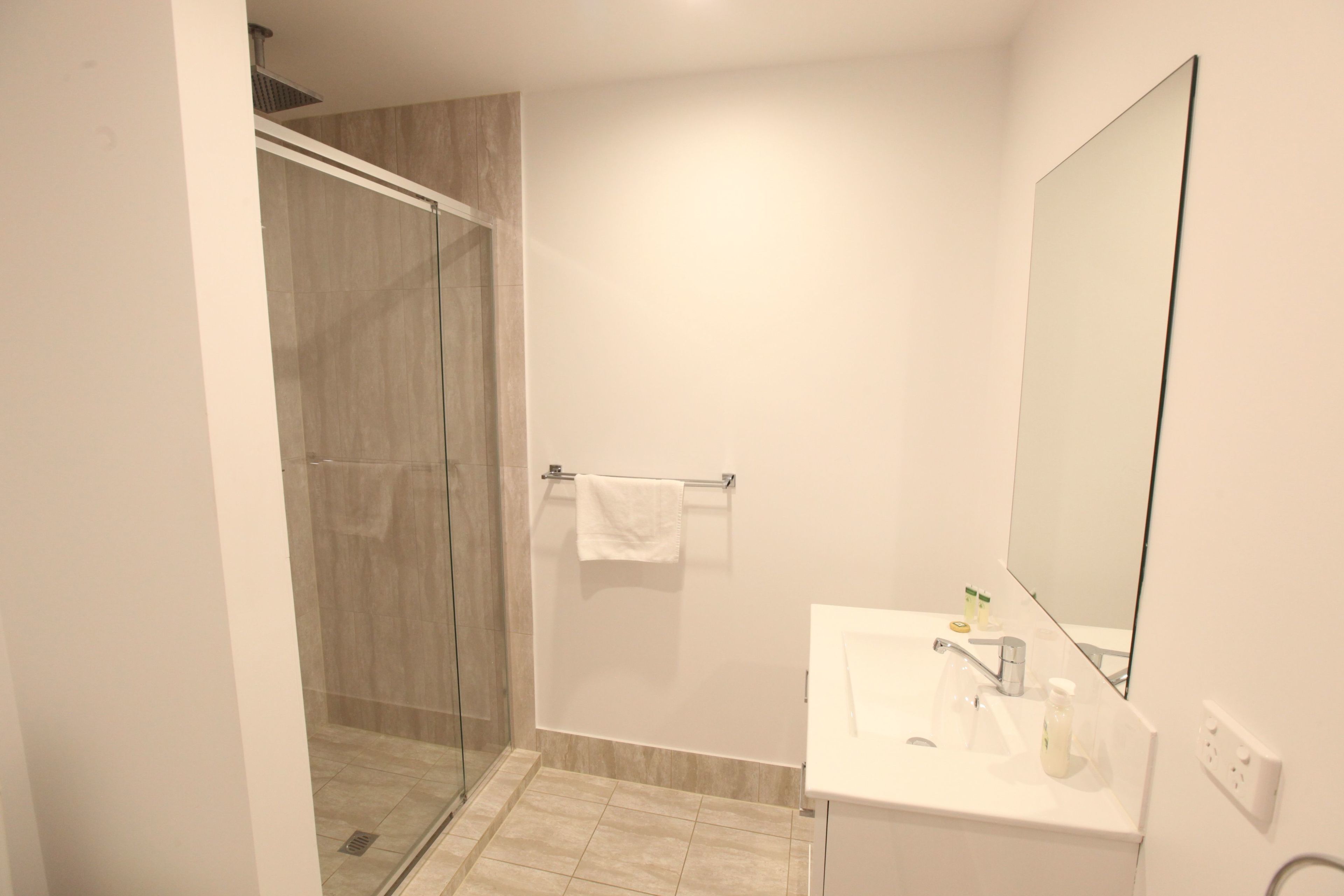 Un baño moderno con cabina de ducha de vidrio, un lavabo blanco con espejo y un perchero para toallas.