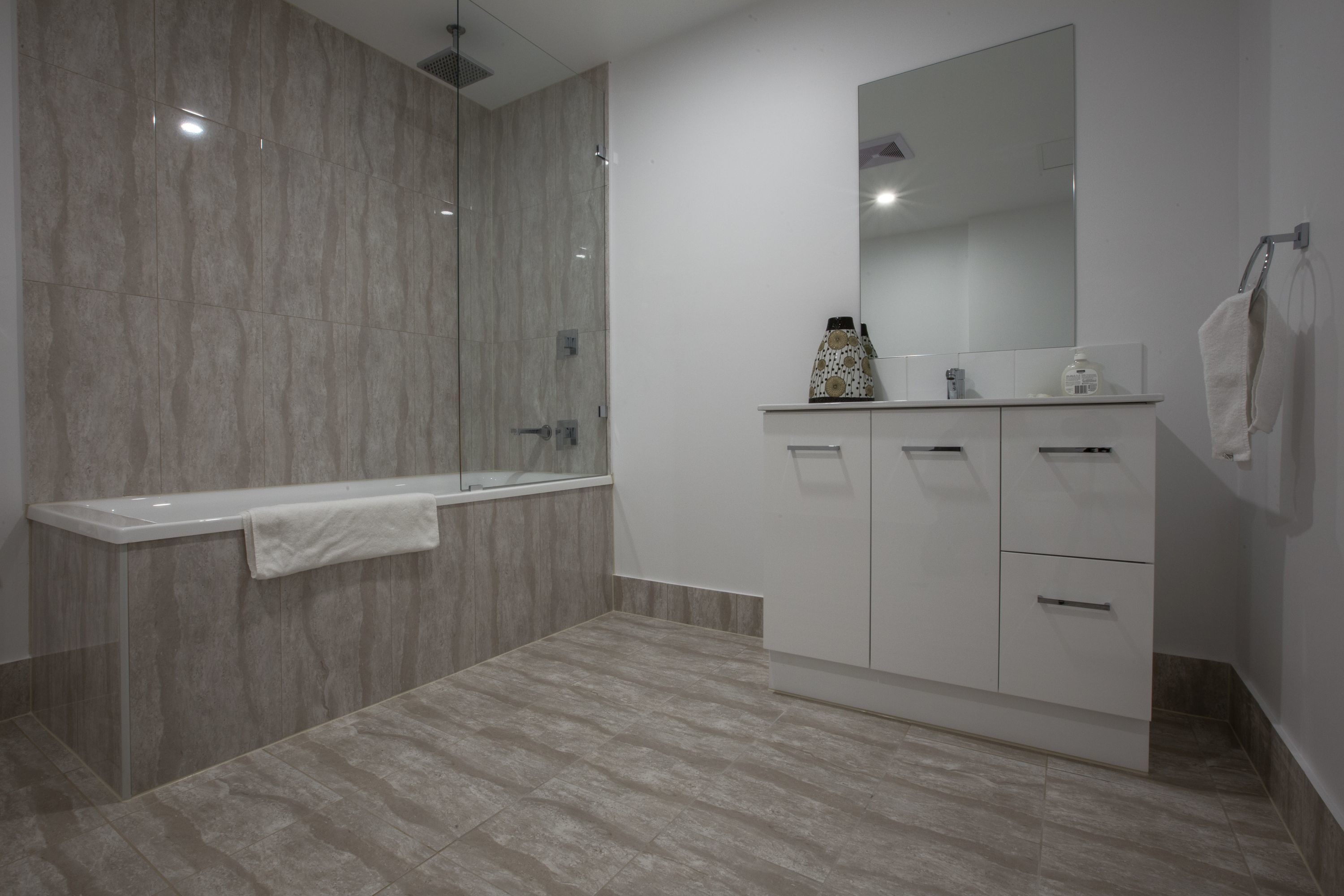 Un baño moderno con ducha envuelta en cristal, tocador blanco con un espejo grande, y una toalla colgada en la pared.