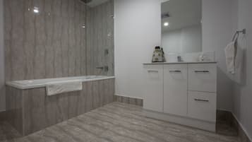 Un baño moderno con ducha envuelta en cristal, tocador blanco con un espejo grande, y una toalla colgada en la pared.