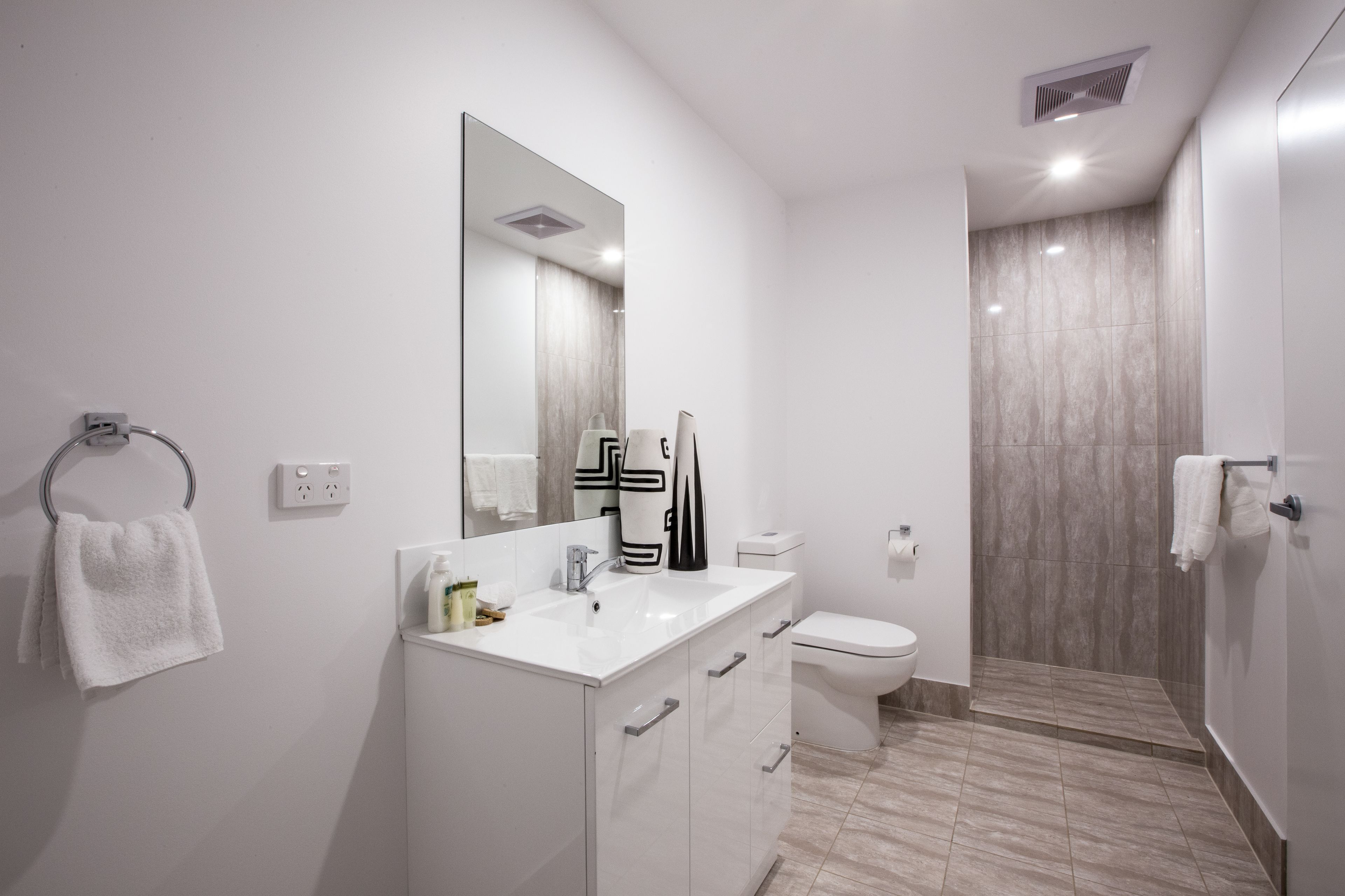 A modern bathroom with a white vanity, a large mirror, a toilet, and a shower area.