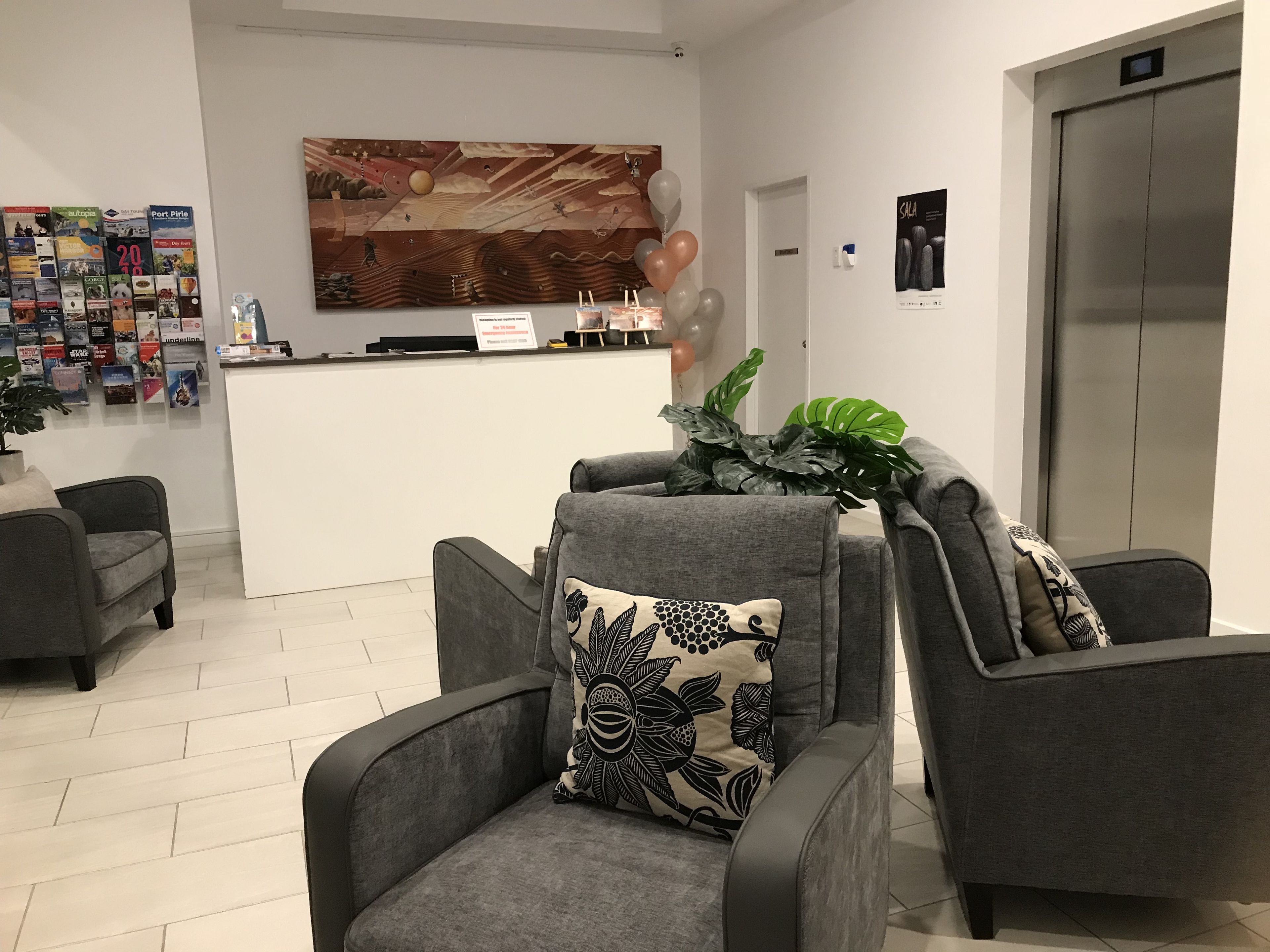 Un área de recepción con un mostrador, un mural grande en la pared y dos sillones grises con cojines estampados.