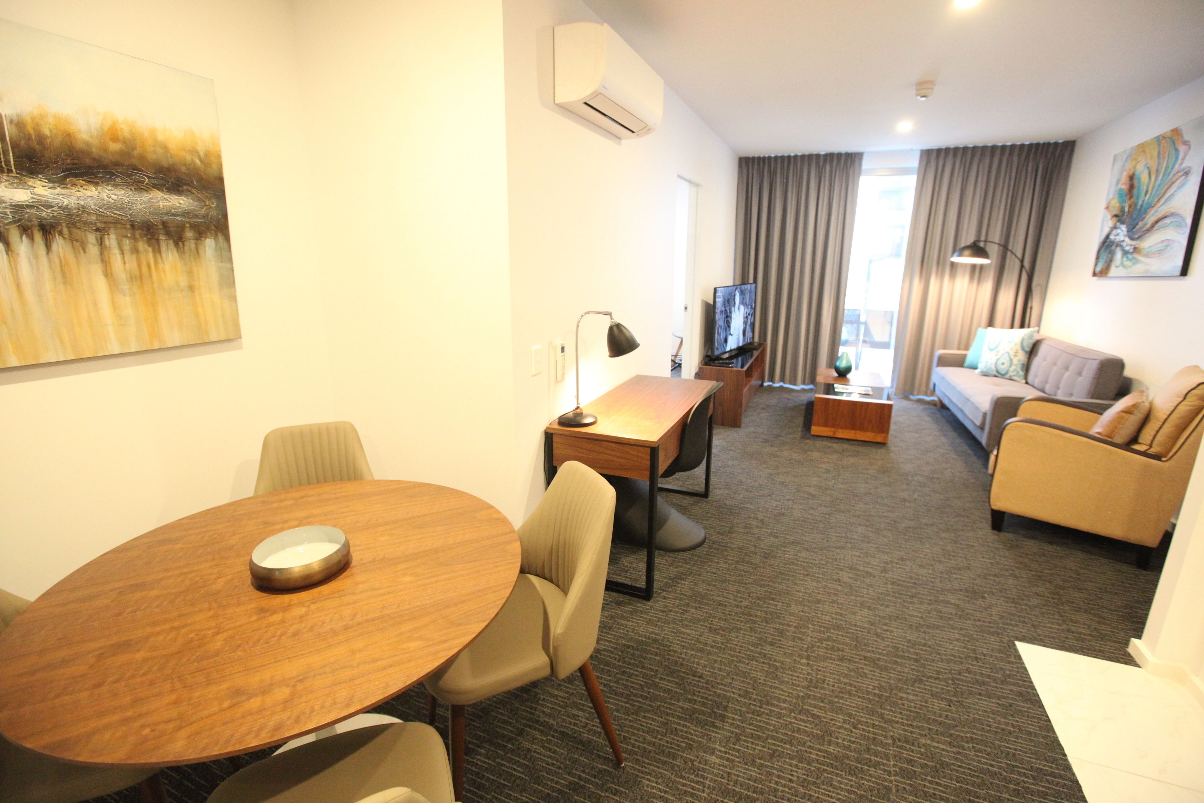 Een hotelkamer met een ronde houten tafel, een bank, een televisie en een schilderij aan de muur.