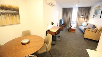 Een hotelkamer met een ronde houten tafel, een bank, een televisie en een schilderij aan de muur.
