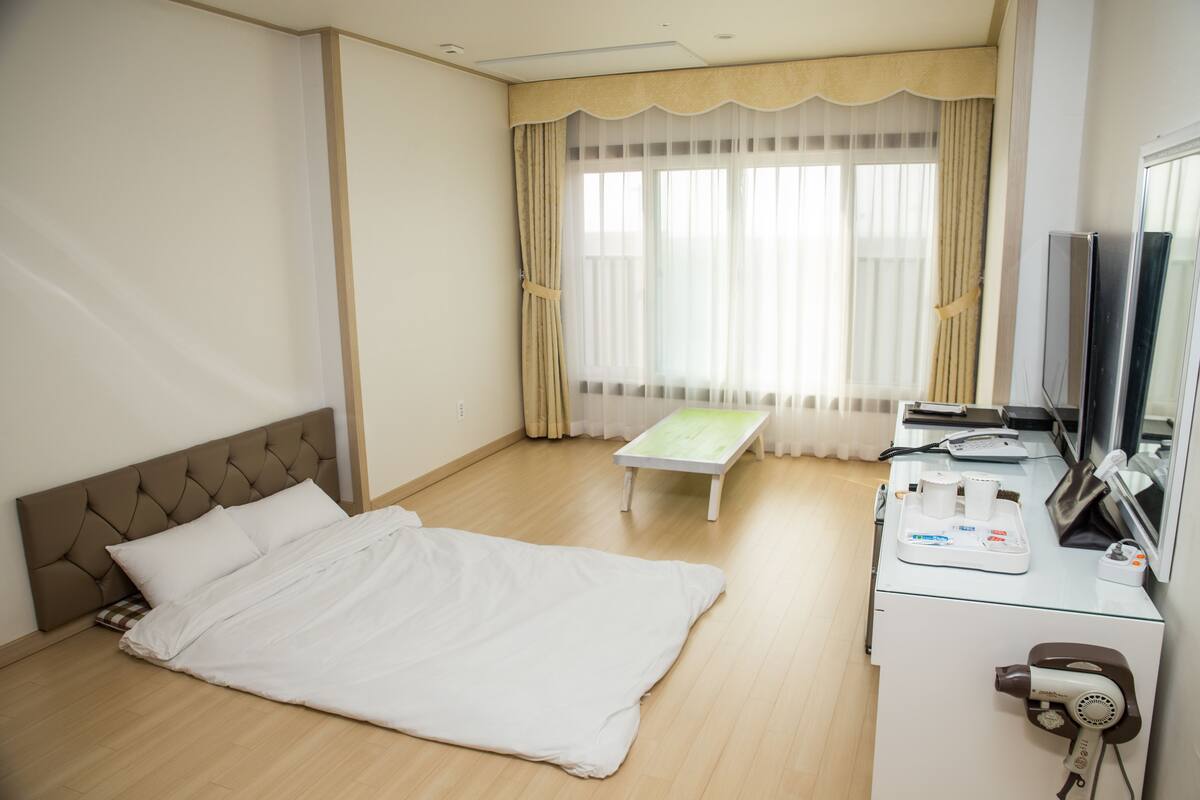 A hotel room with a bed, a bedside table, a TV, and a hairdryer.