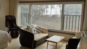 A hotel room with a sofa, armchair, and a small table. There is a large window with a view of trees and buildings outside. - Daebudo Hotel Marina (Ansan)