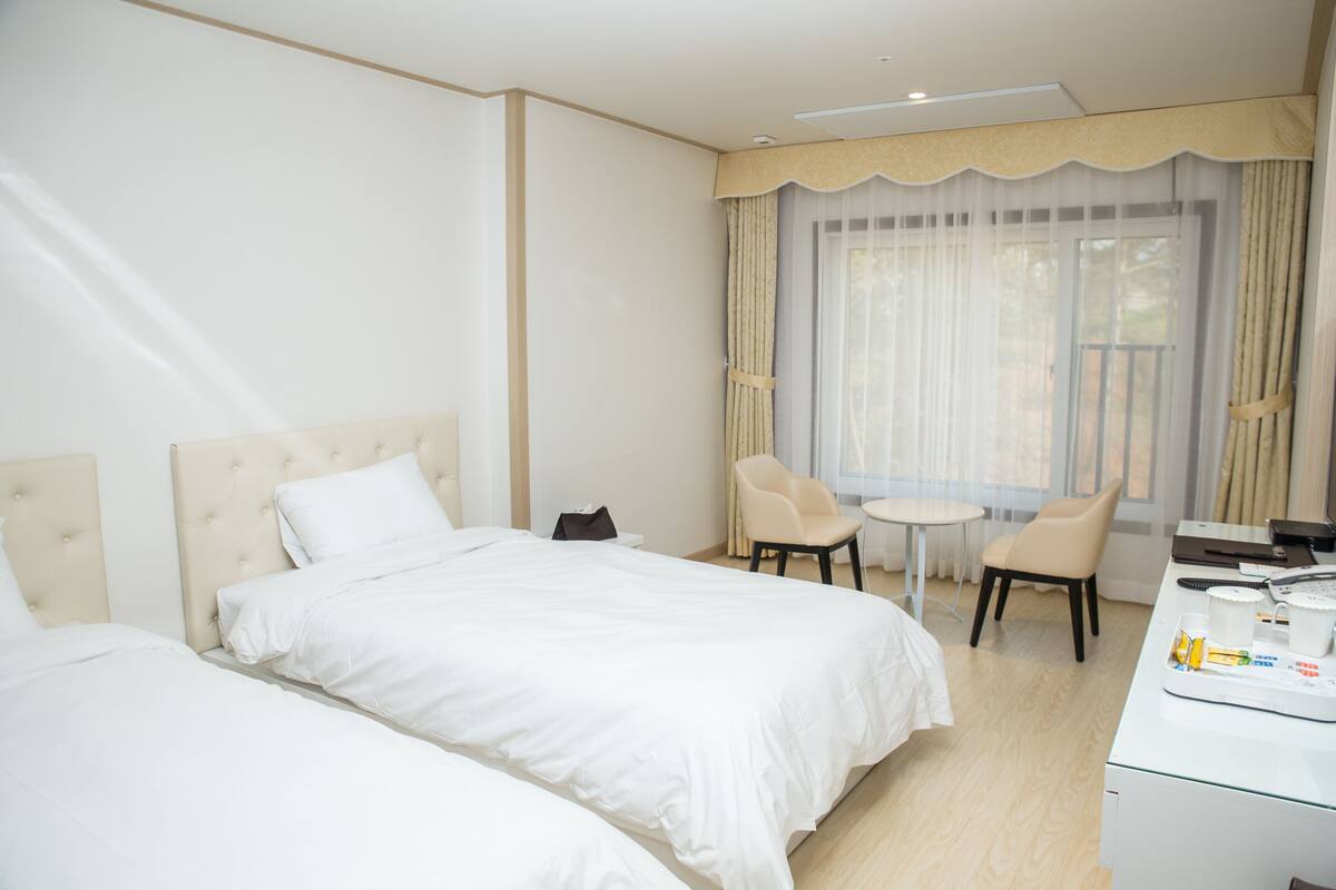 A hotel room with two beds, a desk, a chair, and a small table.