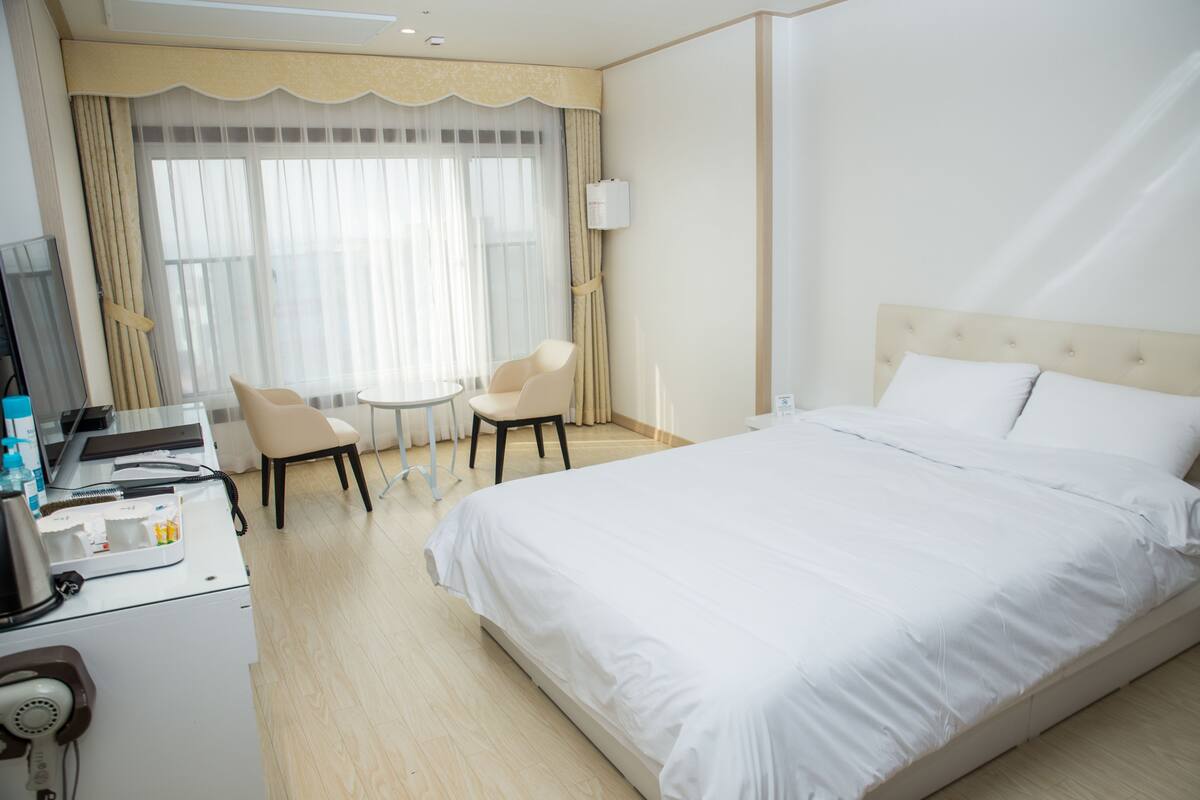 A hotel room with a large bed, a desk with a computer, a chair, and a small table.