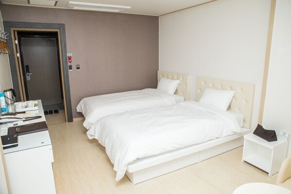 A hotel room with a bed, a desk with a computer, a chair, and a small table with a lamp.