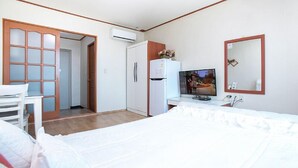 Habitación de hotel con una cama, un escritorio, un televisor, un refrigerador y un espejo.