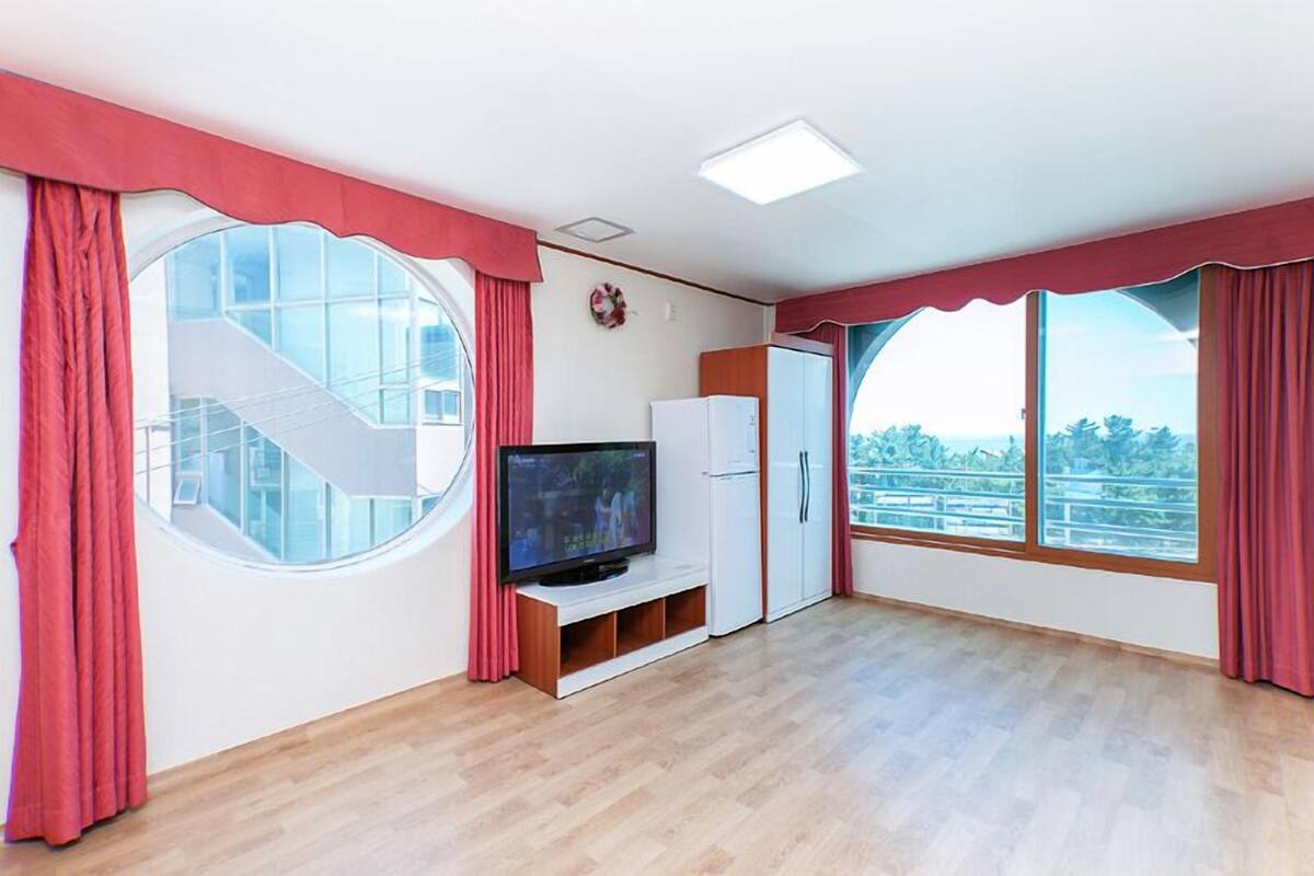 A spacious room with a large window, a television, and a wardrobe.