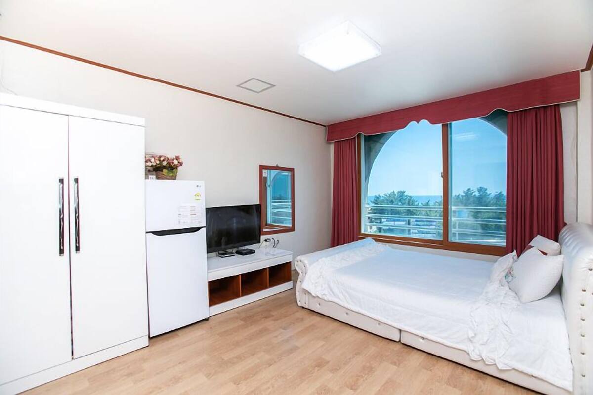 A bedroom with a bed, a TV, a wardrobe, and a window with curtains.