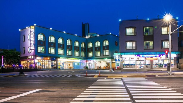 Una intersección con paso de peatones, edificios con letreros iluminados y un semáforo.
