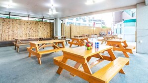 Un amplio espacio exterior con mesas de picnic de madera y un muro de bambú.