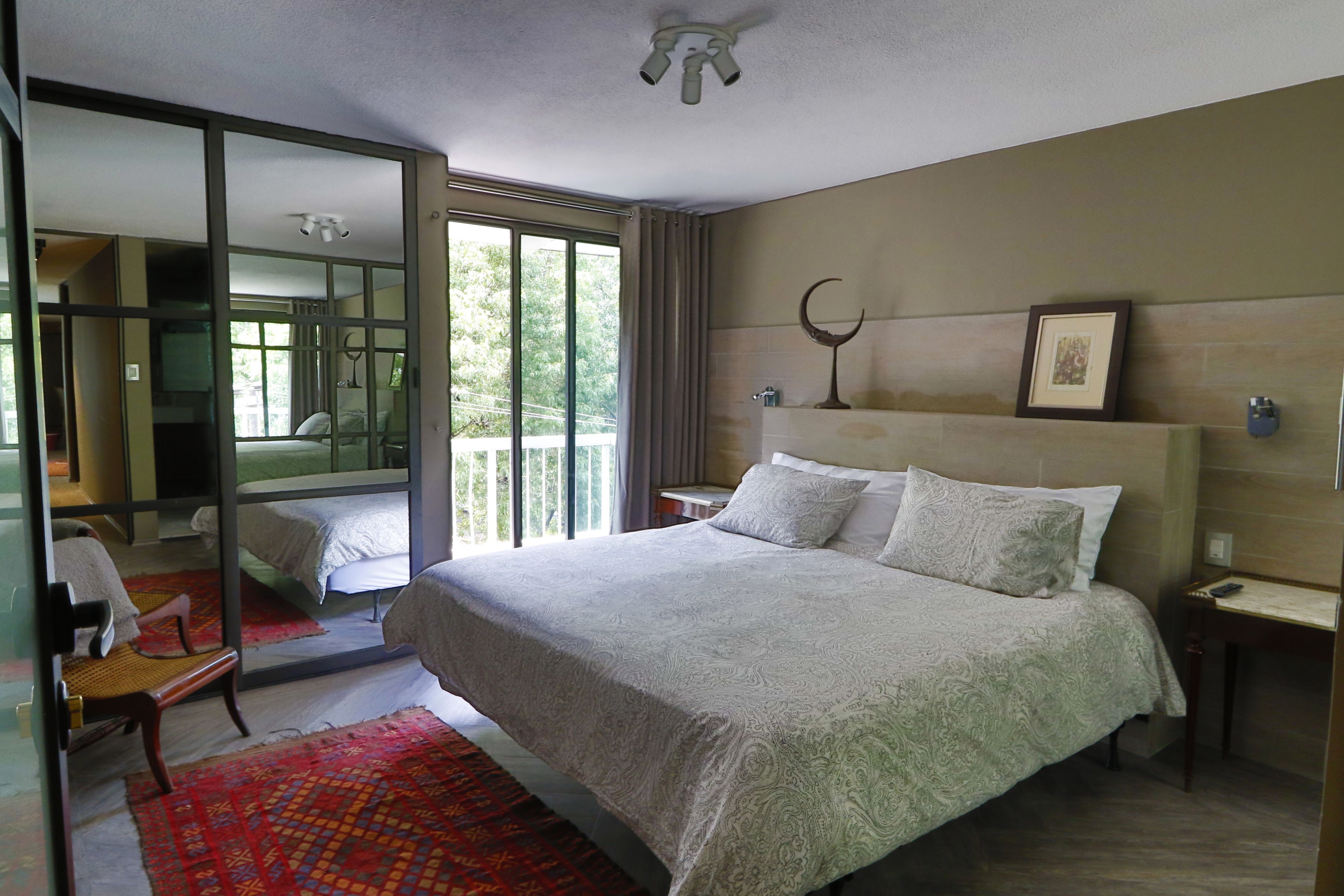 Een moderne hotelkamer met een groot bed, een zithoek met een stoel, een kleine tafel en een groot raam met uitzicht op groen.