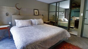 A modern bedroom with a large bed, a nightstand, a wall-mounted clock, and a sliding glass door leading to a bathroom. - Aikia City CDMX (Mexico City)