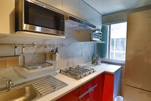 A modern kitchen with stainless steel appliances, a marble backsplash, and red cabinetry. - Aikia City CDMX (Mexico City)