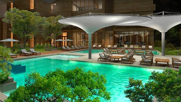A modern pool area with lounge chairs and umbrellas, surrounded by greenery and a building with large windows. - Hotel Maestro (Anseong)