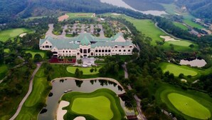 A large, historic building with a symmetrical facade, surrounded by well-manicured golf courses and a central pond. - Hotel Maestro (Anseong)