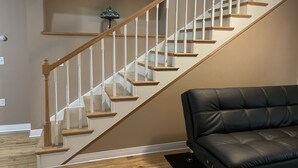 A staircase with wooden steps and white balusters, a black leather sofa, and a small table lamp. - A Little Piece of Relaxation (Millport)