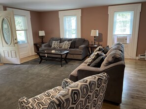 A living room with a sofa, armchair, and coffee table, featuring a patterned throw and decorative pillows.