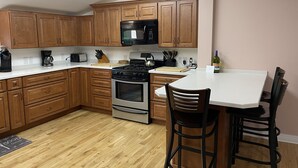 A kitchen with wooden cabinets, a stove, a microwave, and a dining area with two chairs. - A Little Piece of Relaxation (Millport)