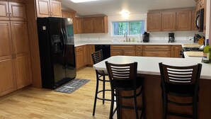 A modern kitchen with wooden cabinets, a black refrigerator, a large island with bar stools, and a window providing natural light. - A Little Piece of Relaxation (Millport)