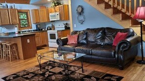 A living room with a leather sofa, a glass coffee table, and a patterned rug. - Hot Tub, River Views, Couples & Families!!! (Burnsville)