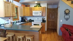 A kitchen with wooden cabinets, a white stove, and a bar area with stools. - Hot Tub, River Views, Couples & Families!!! (Burnsville)