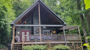 A cabin with a wooden deck, a red door, and a balcony with chairs. - Hot Tub, River Views, Couples & Families!!! (Burnsville)