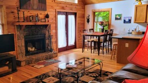 A cozy cabin interior with a stone fireplace, wooden walls, a dining area, and a kitchen. - Hot Tub, River Views, Couples & Families!!! (Burnsville)