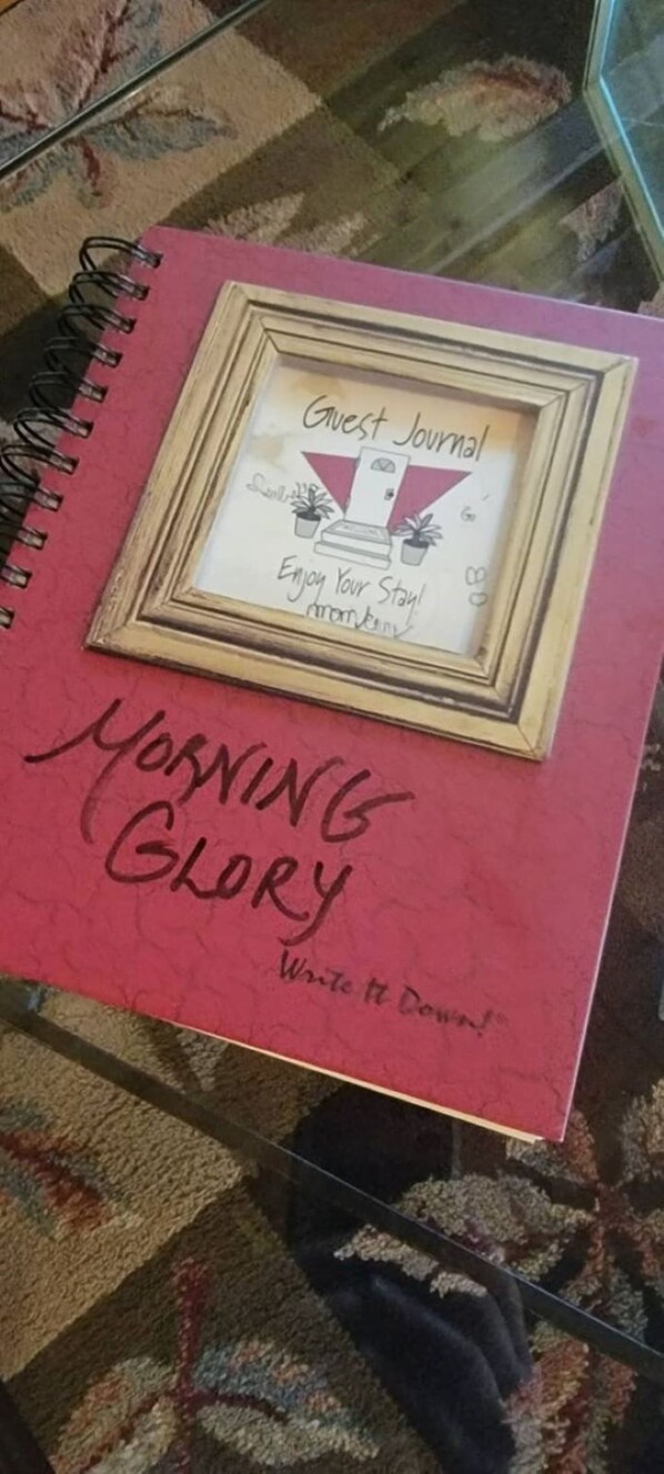 A red notebook with 'Guest Journal' and 'Enjoy Your Stay' written on it, placed on a glass table.