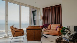 A living room with a view of the ocean, featuring a sofa, two armchairs, a coffee table, and a decorative sculpture. - Apartment in Egmond with Sea Views (Egmond aan zee)